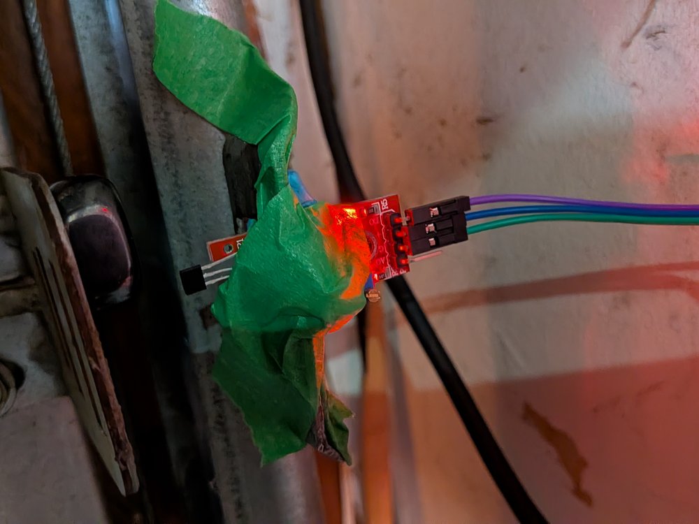 Linear Hall-effect sensor mounted near a garage door track, LED lit indicating the door is detected as closed